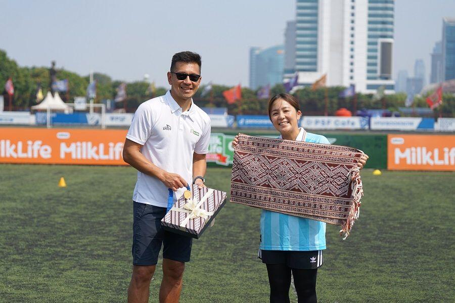 Program Director MilkLife Soccer Challenge, Teddy Tjahjono (baju putih), menyerahkan cinderamata berupa kain tradisional Indonesia kepada Mana Iwabuchi di Pancoran Soccer Field, Jakarta, 3 Agustus 2025. (Istimewa)