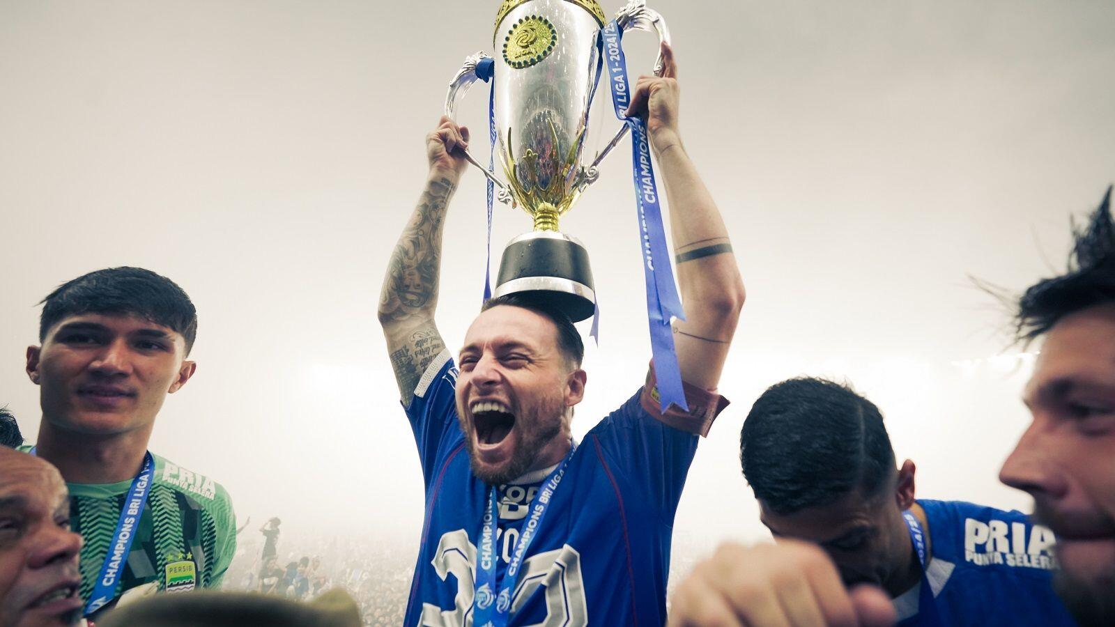 Marc Klok merayakan keberhasilan Persib Bandung menjuarai Liga 1 2024-2025 dengan meletakan trofi di atas kepalanya di Stadion Gelora Bandung Lautan Api (GBLA), Bandung, 24 Mei 2025. (Yogie Gandanaya/Skor.id)