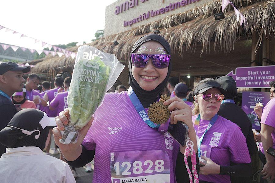 Aprisa pelari dari Bandung memamerkan medali dan sayur yang ia dapatkan di Amartha 10X Run 2025. (Foto: Yogie Gandanaya/Skor.id)